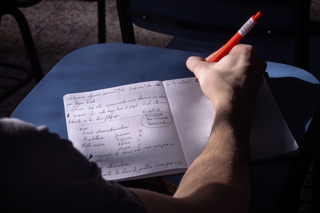 A student takes notes in a classroom in Buenos Aires. Natural lighting highlights the writing process.