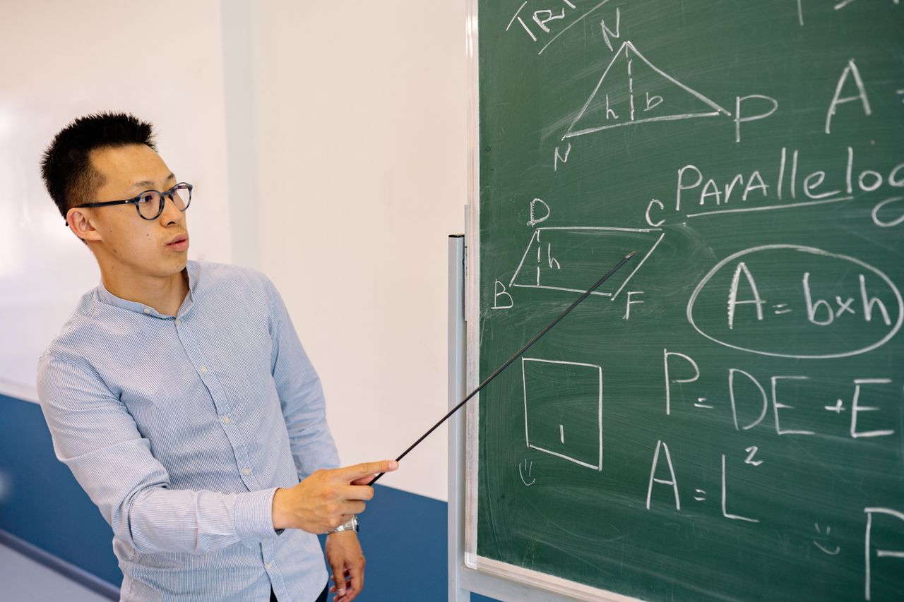 Math teacher demonstrating equations on the blackboard in classroom setting.