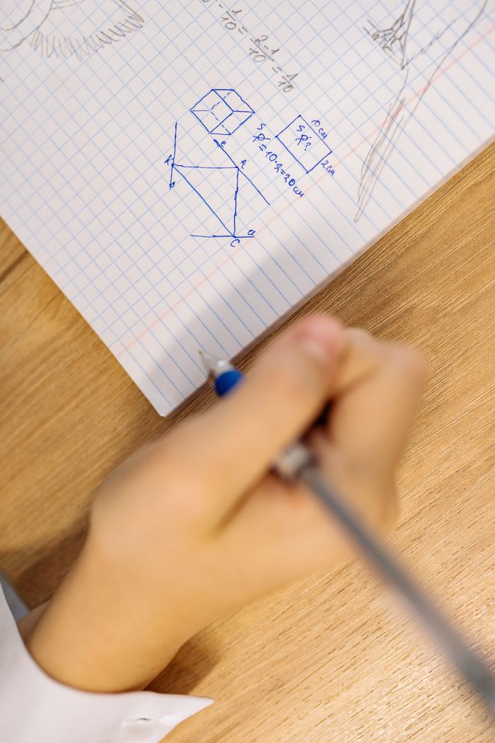 Hand writing math equations in a notebook, focusing on geometric drawings and study.